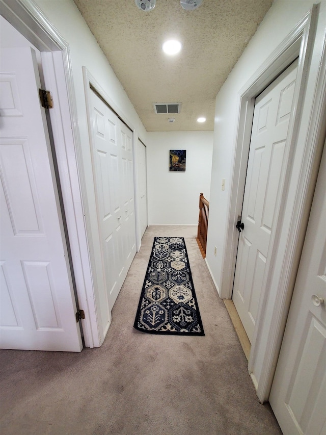 corridor with light carpet, visible vents, and a textured ceiling