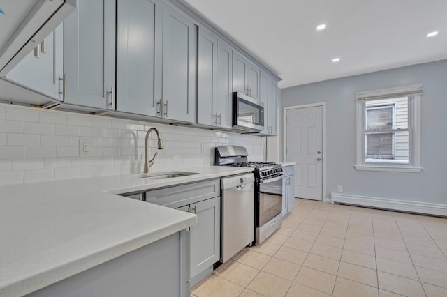 kitchen with gray cabinets, light tile patterned flooring, a baseboard heating unit, and appliances with stainless steel finishes