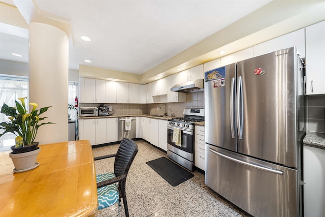 kitchen with appliances with stainless steel finishes, a sink, under cabinet range hood, white cabinetry, and backsplash
