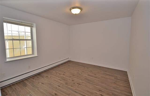55 71st St, Guttenberg, NJ 07093 - empty room with a baseboard heating unit, wood finished floors, and baseboards