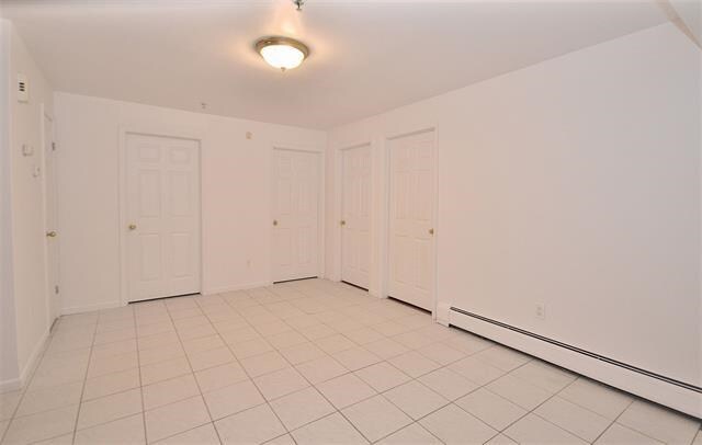 55 71st St, Guttenberg, NJ 07093 - unfurnished bedroom with a baseboard heating unit, light tile patterned floors, and baseboards