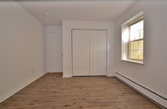 55 71st St, Guttenberg, NJ 07093 - unfurnished bedroom with baseboard heating, wood finished floors, a closet, and baseboards