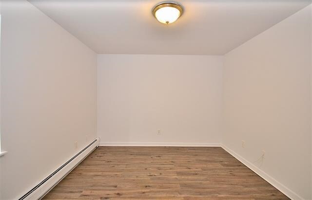 55 71st St, Guttenberg, NJ 07093 - empty room featuring a baseboard heating unit, wood finished floors, and baseboards