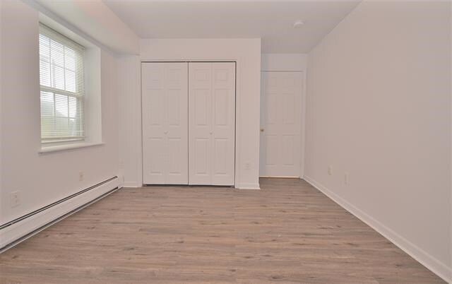 55 71st St, Guttenberg, NJ 07093 - unfurnished bedroom with baseboard heating, wood finished floors, a closet, and baseboards