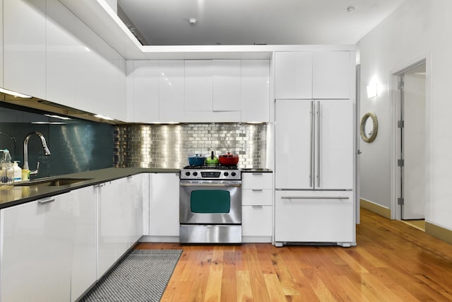 kitchen with sink, paneled built in refrigerator, white cabinetry, light hardwood / wood-style floors, and stainless steel range with gas cooktop