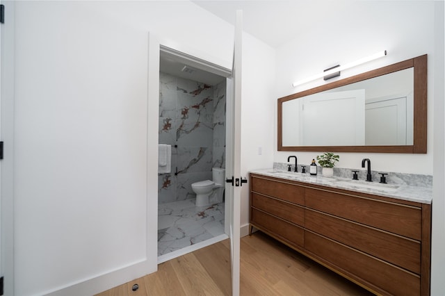 full bath with double vanity, wood finished floors, a sink, and toilet