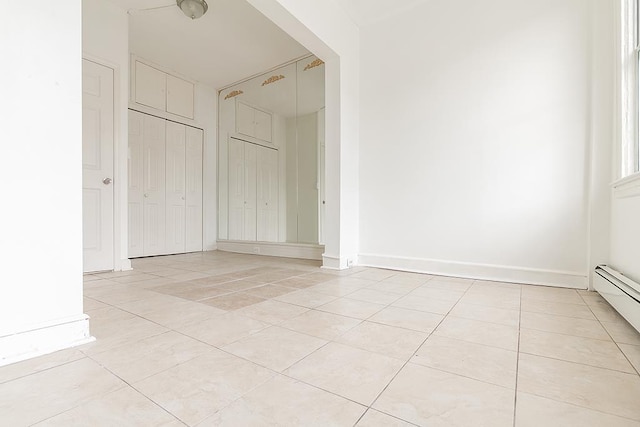 interior space with a baseboard heating unit, baseboards, a closet, and light tile patterned floors