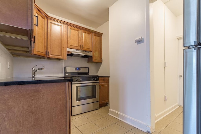 kitchen featuring light tile patterned flooring, dark countertops, gas stove, brown cabinets, and under cabinet range hood