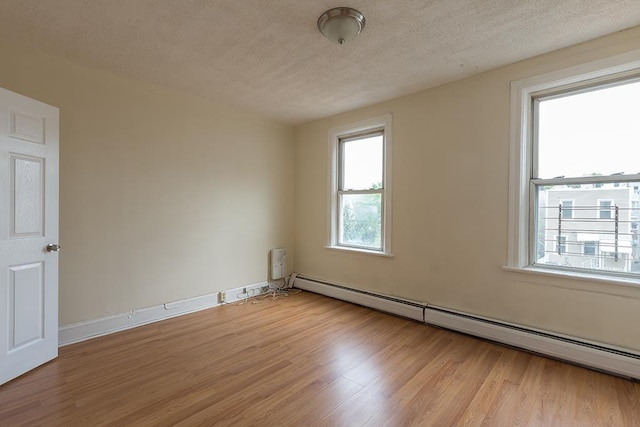 unfurnished room with plenty of natural light, baseboard heating, and wood finished floors