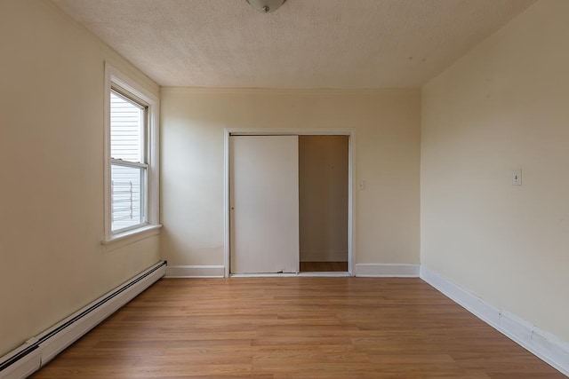 spare room featuring a baseboard heating unit, baseboards, a textured ceiling, and light wood-style floors