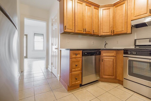 kitchen with stainless steel appliances, under cabinet range hood, light tile patterned floors, and tasteful backsplash