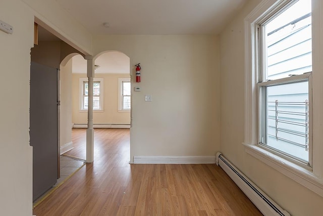 spare room featuring baseboard heating, arched walkways, light wood-style floors, and baseboards