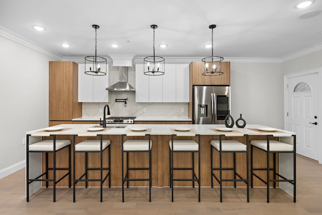 kitchen featuring white cabinets, stainless steel fridge, a center island with sink, and wall chimney exhaust hood