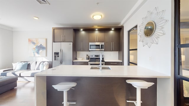 kitchen featuring stainless steel appliances, a kitchen bar, wood-type flooring, and dark brown cabinets