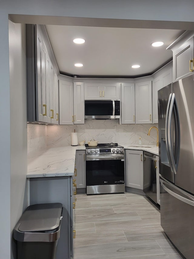 kitchen featuring gray cabinetry, decorative backsplash, light stone countertops, and appliances with stainless steel finishes