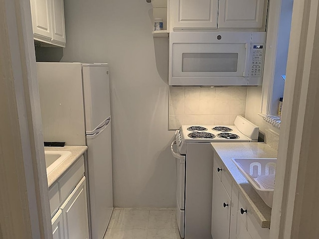 kitchen with white appliances, backsplash, white cabinets, and light countertops