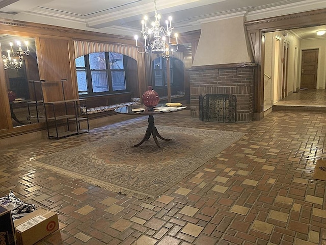 interior space featuring beam ceiling, brick floor, ornamental molding, a brick fireplace, and a notable chandelier