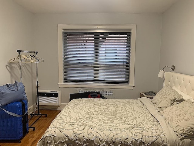 bedroom with a wall mounted air conditioner, baseboards, and wood finished floors