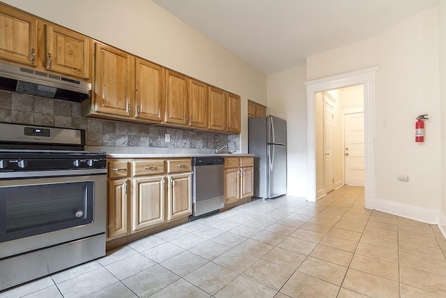 kitchen featuring decorative backsplash, brown cabinets, stainless steel appliances, under cabinet range hood, and light tile patterned flooring