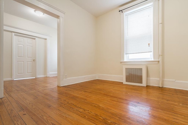 empty room featuring baseboards, light wood-style flooring, and radiator heating unit