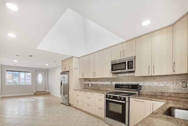 kitchen with stone countertops, cream cabinets, backsplash, and appliances with stainless steel finishes