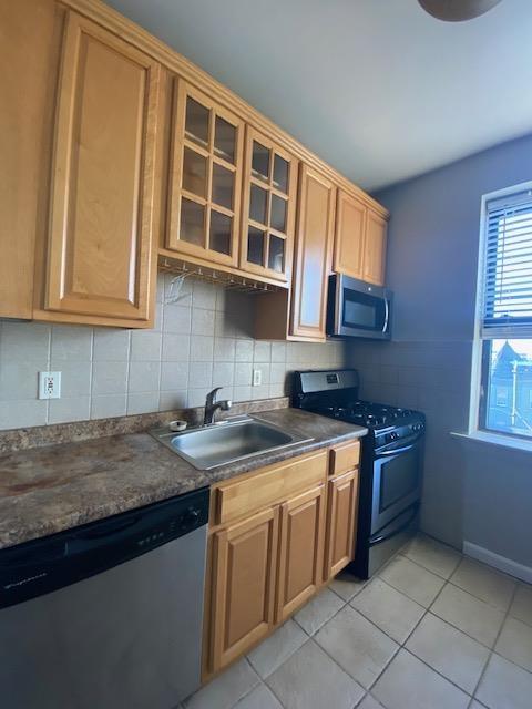680 Kennedy Blvd Unit 406, Bayonne, NJ 07002 - kitchen featuring appliances with stainless steel finishes, a sink, dark countertops, light tile patterned floors, and glass insert cabinets