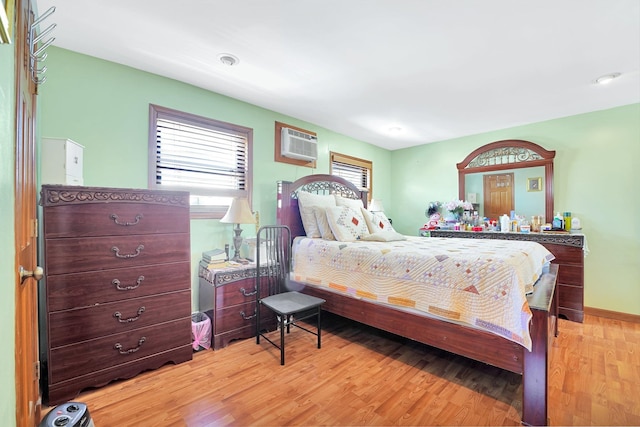 bedroom with an AC wall unit, light wood-type flooring, and baseboards