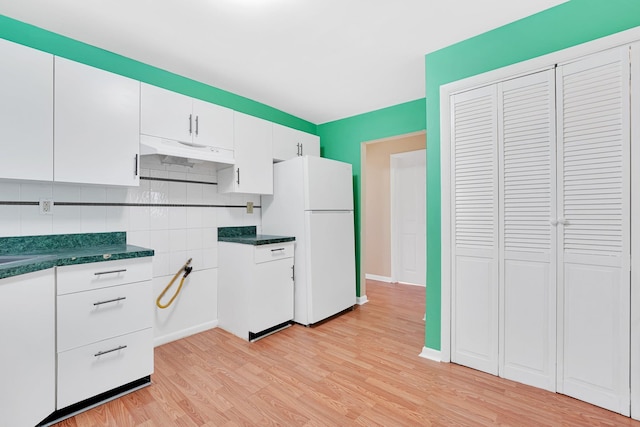 kitchen featuring dark countertops, under cabinet range hood, light wood-type flooring, freestanding refrigerator, and white cabinetry