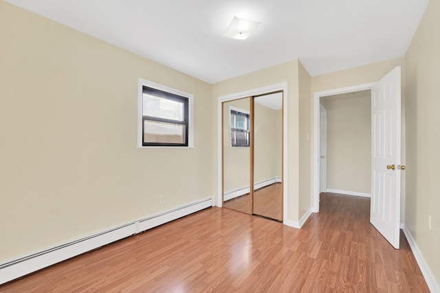 unfurnished bedroom with a baseboard heating unit, baseboards, light wood-type flooring, baseboard heating, and a closet