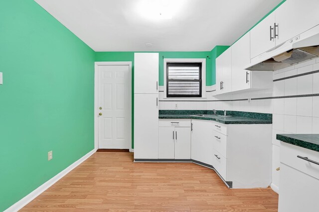 kitchen with dark countertops, white cabinets, light wood-type flooring, and a sink