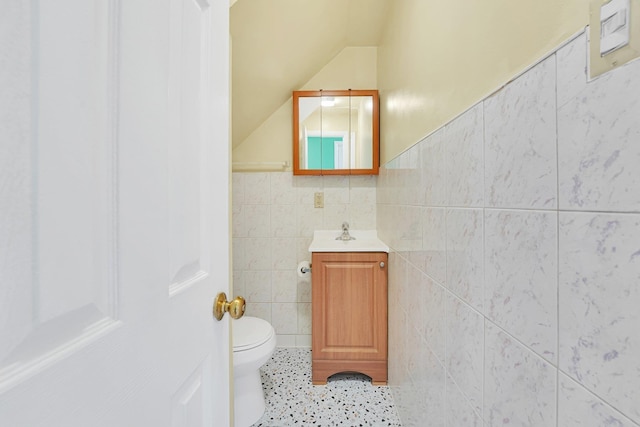 bathroom with tile patterned floors, toilet, tile walls, vanity, and vaulted ceiling