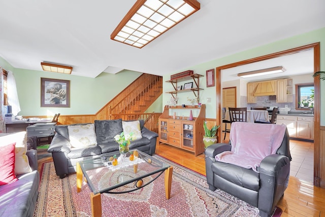 living room featuring stairs, light wood finished floors, a wainscoted wall, and wood walls