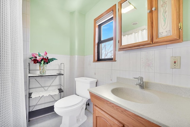 full bathroom with vanity, a wainscoted wall, tile patterned floors, toilet, and tile walls