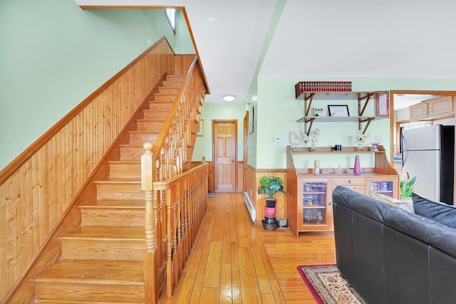 stairs featuring a baseboard heating unit, hardwood / wood-style floors, wainscoting, and wood walls