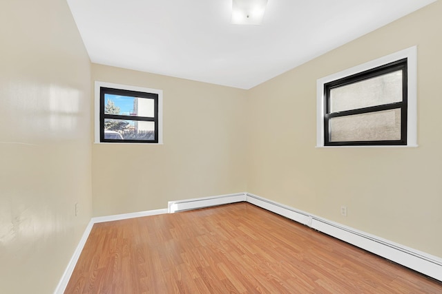 empty room featuring a baseboard radiator, baseboards, and wood finished floors