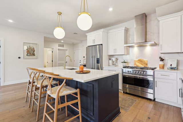 kitchen with high quality appliances, light wood-style flooring, a sink, light countertops, and wall chimney exhaust hood