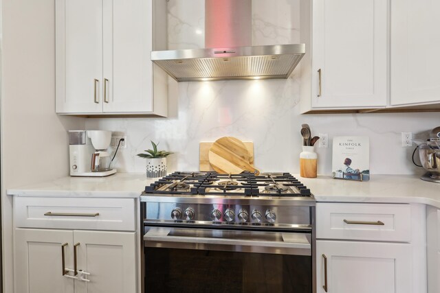 kitchen featuring light stone countertops, island exhaust hood, high end stove, white cabinetry, and tasteful backsplash