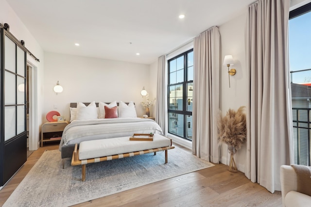 bedroom with recessed lighting, light wood-type flooring, and a barn door