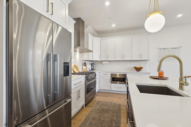 kitchen featuring light wood-style flooring, white cabinets, stainless steel appliances, wall chimney exhaust hood, and a sink