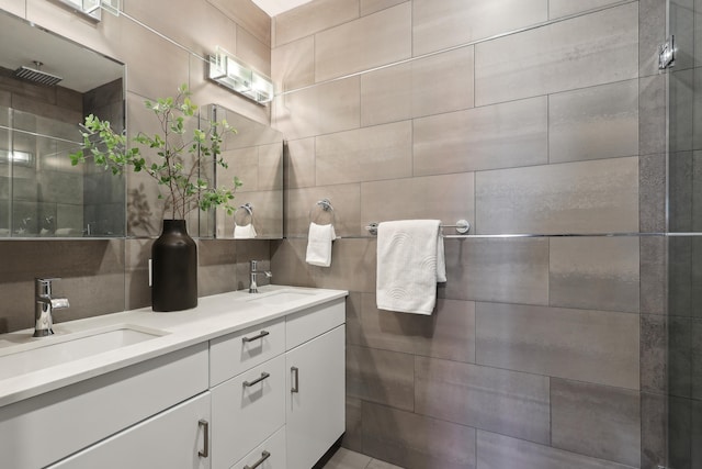 bathroom with a tile shower, double vanity, tile walls, and a sink