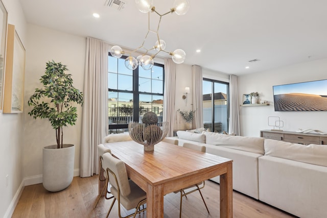 dining room with light wood-type flooring, visible vents, a notable chandelier, and a healthy amount of sunlight