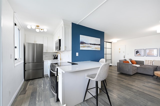 kitchen featuring white cabinetry, appliances with stainless steel finishes, a kitchen bar, and dark wood-type flooring