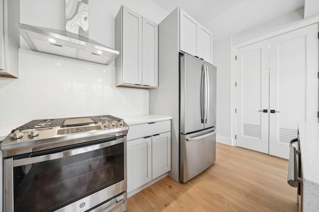 kitchen with stainless steel appliances, tasteful backsplash, wall chimney range hood, and light wood-type flooring