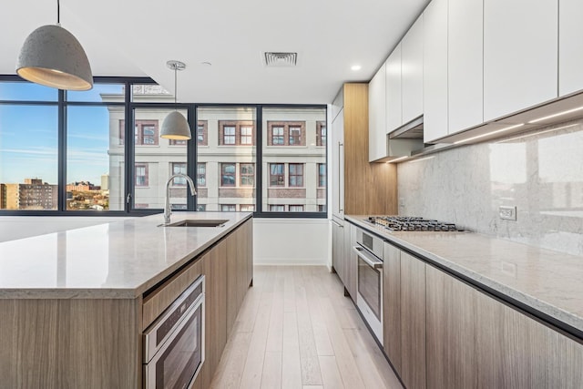 kitchen featuring appliances with stainless steel finishes, light stone counters, sink, decorative light fixtures, and white cabinets