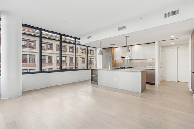 kitchen with tasteful backsplash, pendant lighting, light hardwood / wood-style flooring, white cabinetry, and an island with sink