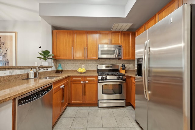 kitchen with backsplash, sink, light stone countertops, light tile patterned floors, and stainless steel appliances