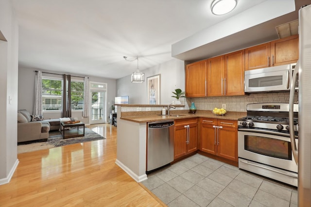 kitchen featuring pendant lighting, sink, appliances with stainless steel finishes, kitchen peninsula, and a chandelier