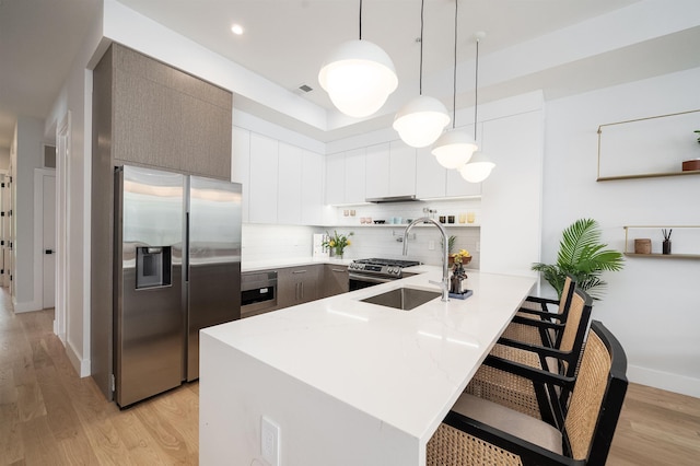 kitchen featuring pendant lighting, white cabinets, a kitchen bar, kitchen peninsula, and stainless steel appliances