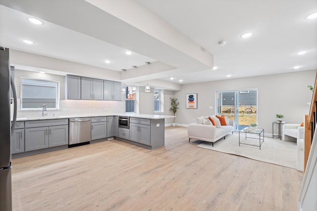 kitchen with a peninsula, open floor plan, appliances with stainless steel finishes, light wood-type flooring, and gray cabinets