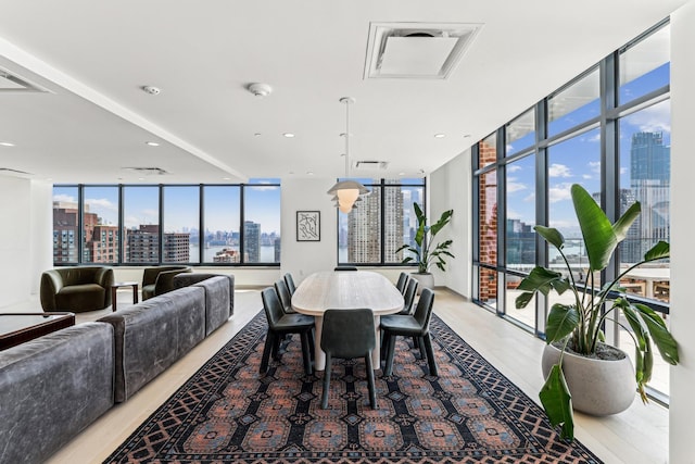 dining space featuring light wood-type flooring, visible vents, a view of city, floor to ceiling windows, and recessed lighting